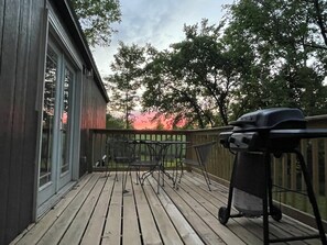 A wooden deck with a grill, a table, and chairs, overlooking a forested area.