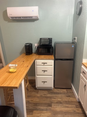 A compact kitchenette with a microwave, toaster, and refrigerator, a wooden countertop, and a white cabinet with drawers.