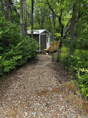 Ein Kiesweg führt zu einer Holzterrasse und einer kleinen Gartenhütte im Wald.