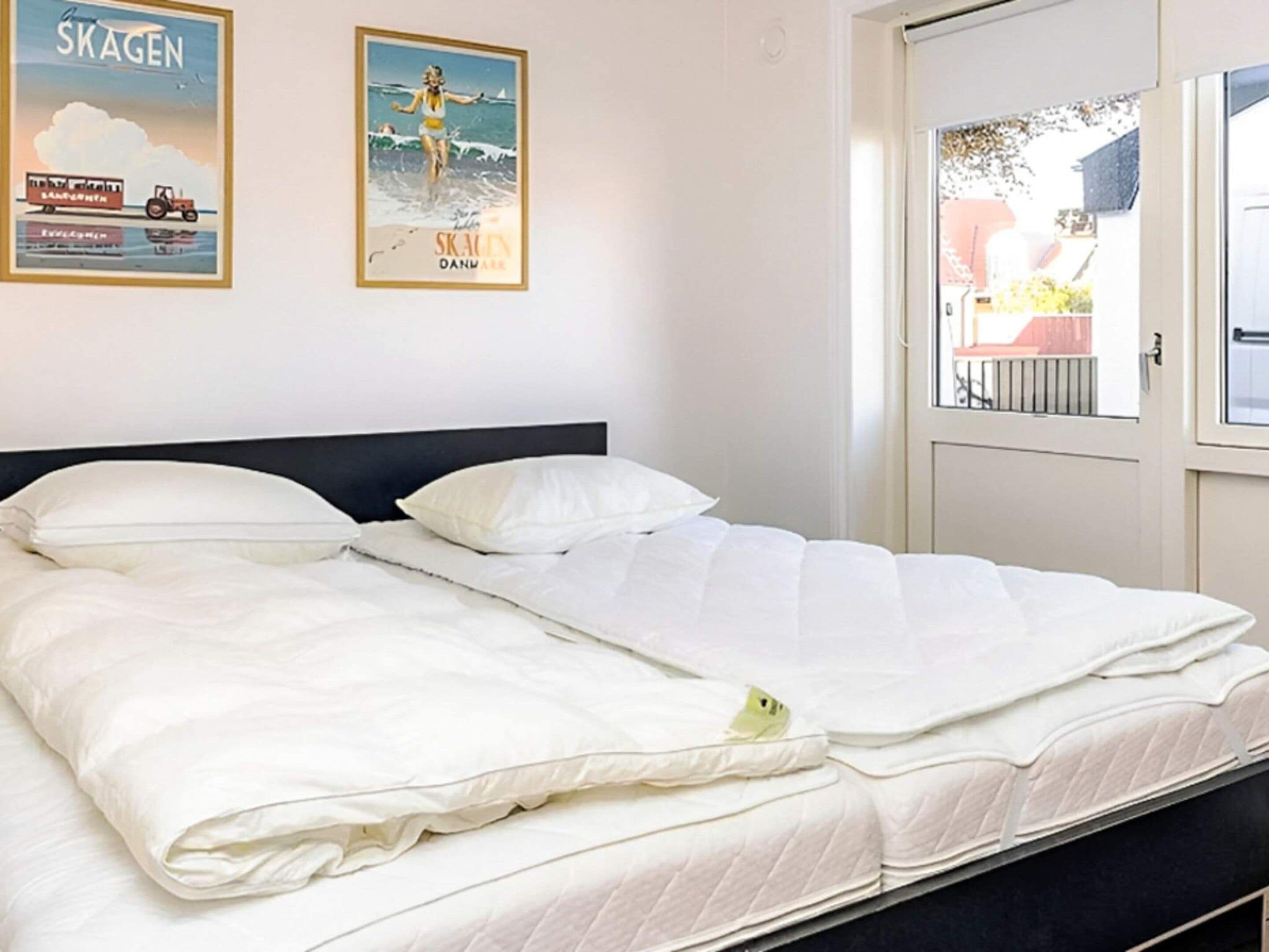 A bed with white bedding in a room with a door and two posters on the wall.
