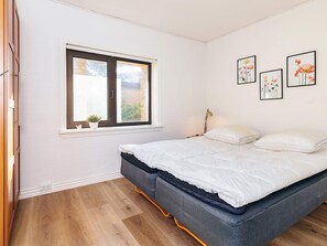 Ein Schlafzimmer mit Bett, Fenster, Nachttisch und Wandbildern.