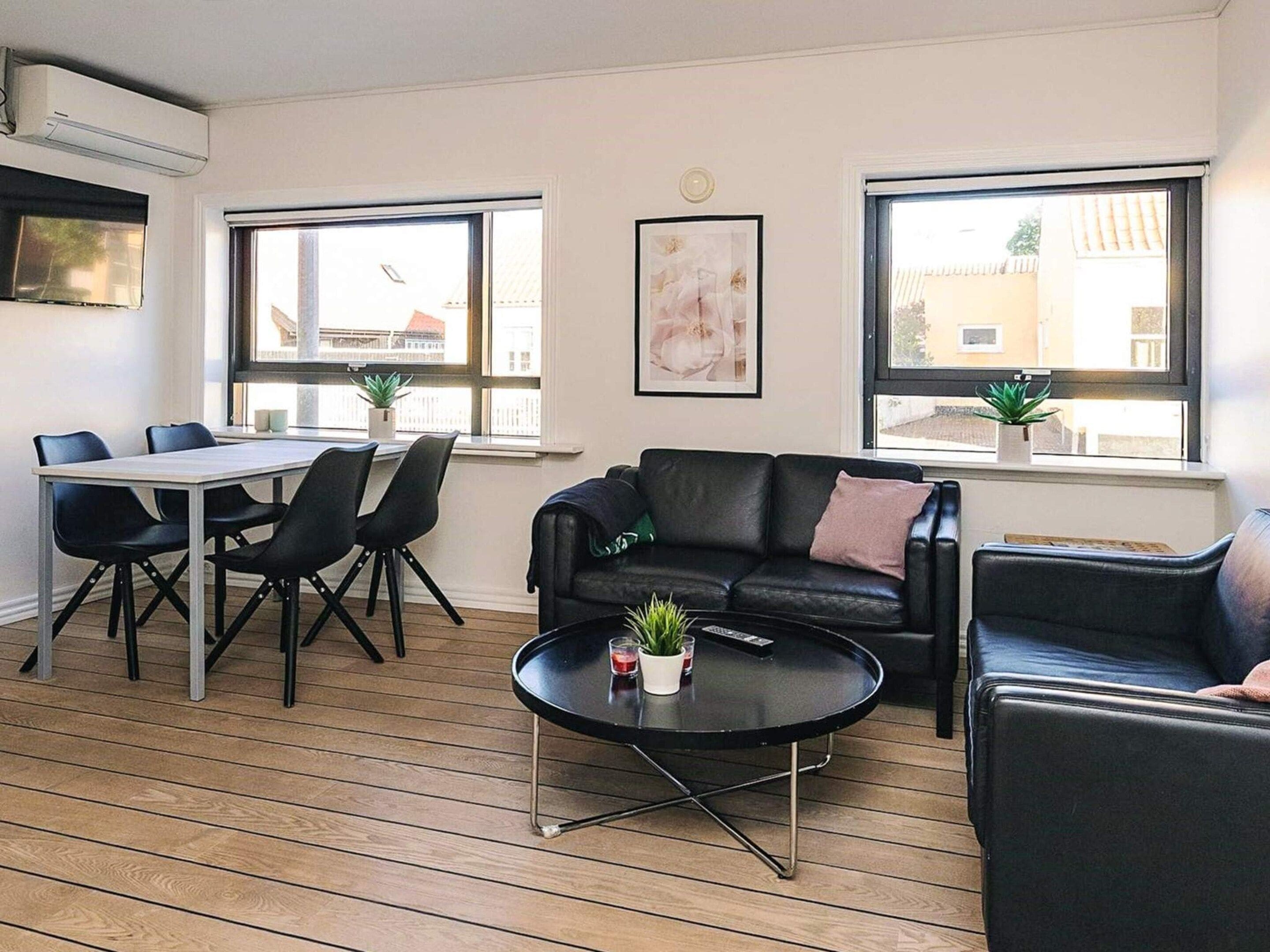 A modern living room with a black leather sofa, a round coffee table, and a dining area with a white table and black chairs.