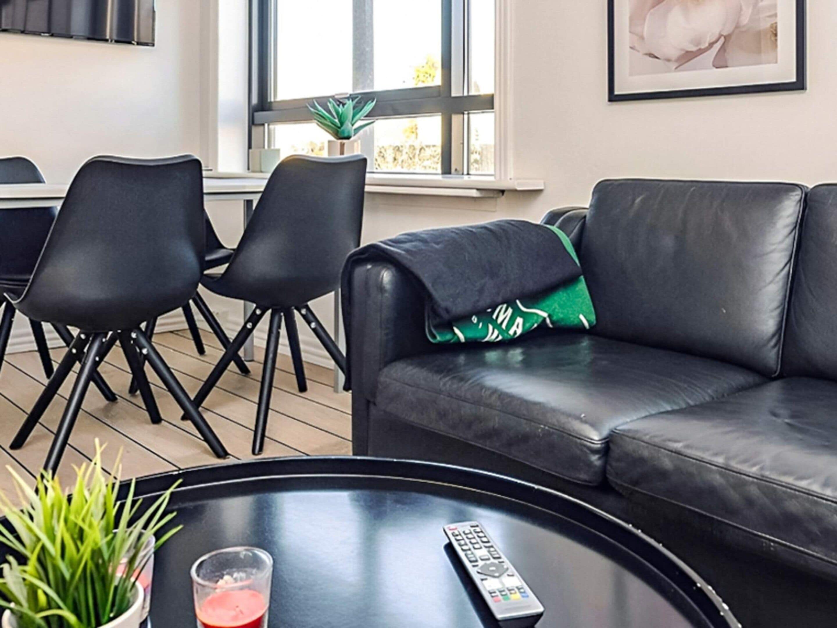 Ein modernes Wohnzimmer mit einem schwarzen Ledersofa, einem schwarzen Couchtisch und einer Fernbedienung.