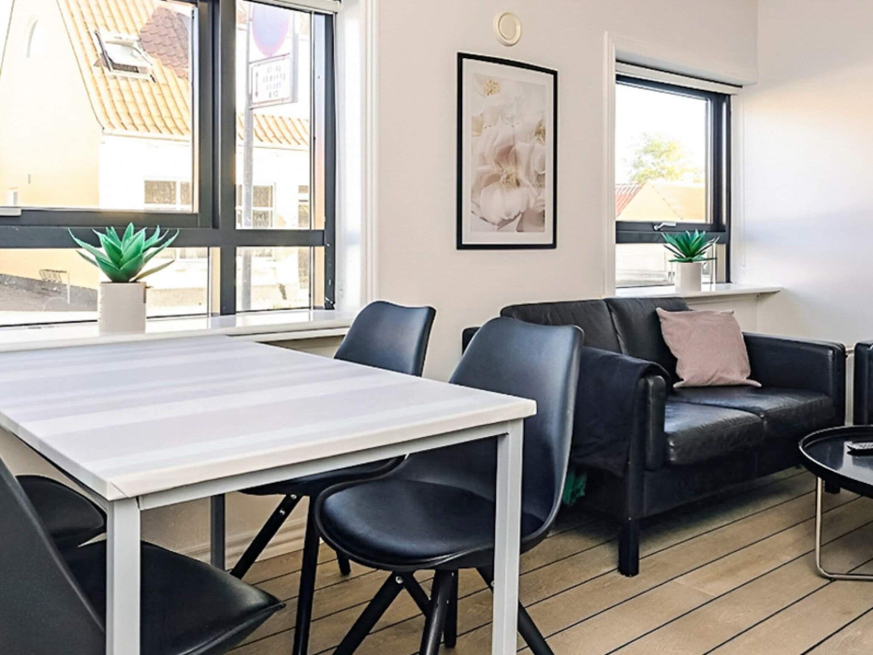A modern room with a white table, black chairs, a black leather sofa, and a window with a view of buildings.