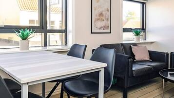 A modern room with a white table, black chairs, a black leather sofa, and a window with a view of buildings.