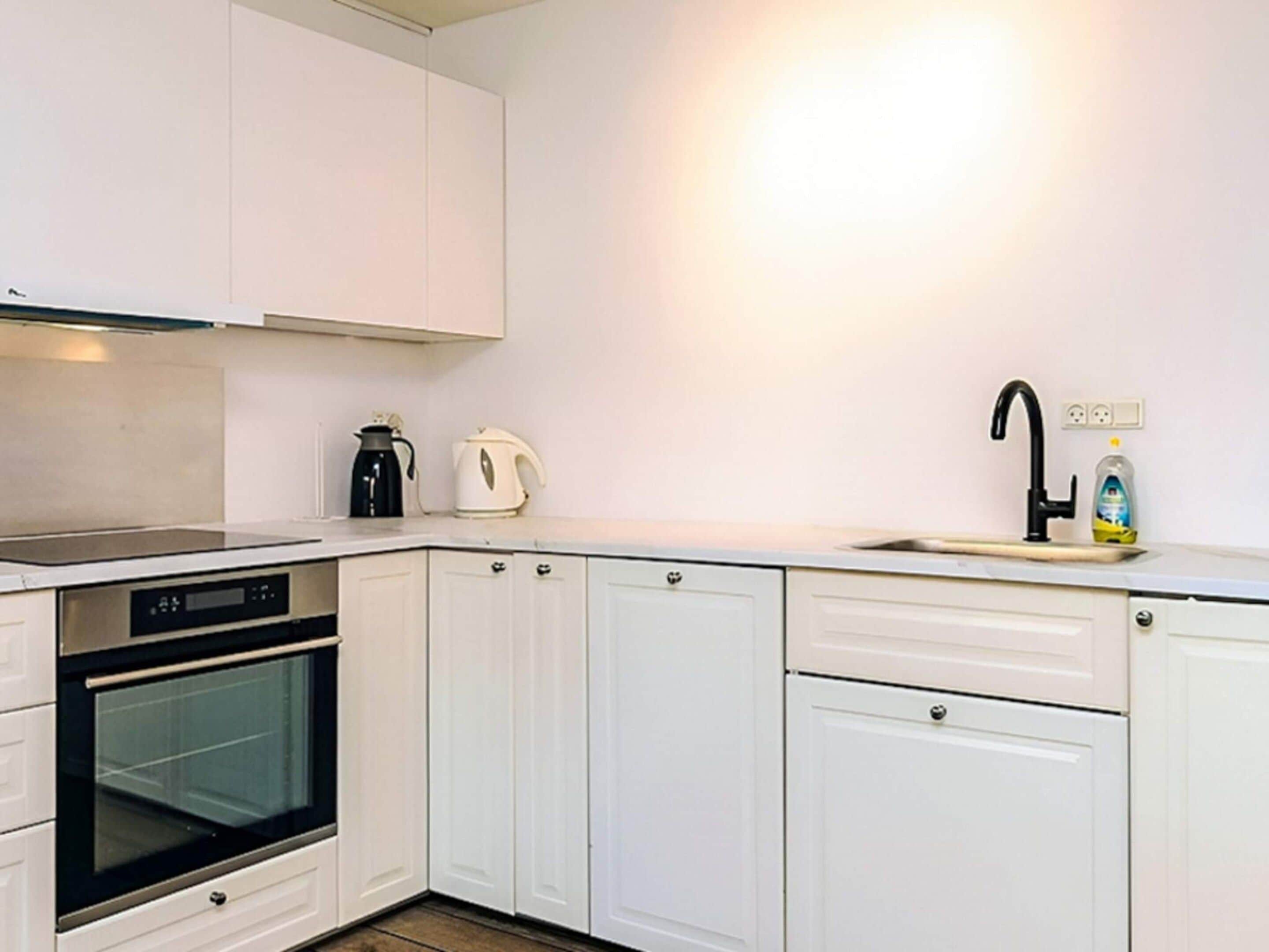 A modern kitchen with white cabinetry, a built-in oven, a coffee maker, and a sink with a faucet.