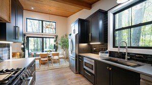 A modern kitchen with dark cabinetry, stainless steel appliances, and a large window offering a view of trees. - New listing! 4BR Holland Getaway Near Lake Michigan Beaches & Kirk Park (West Olive)