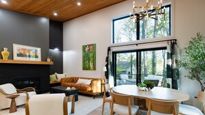 A modern living room with a fireplace, a dining area, and a large window with a view of trees. - New listing! 4BR Holland Getaway Near Lake Michigan Beaches & Kirk Park (West Olive)