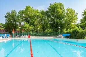 Une piscine à l’eau claire, entourée d’arbres et d’une clôture.