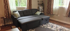 A gray sectional sofa with storage, a small wooden side table, a patterned rug, and a window with curtains. - 2 Acres Private Gated Retreat Near Lake Morton (Kent)