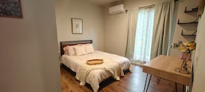 Quarto com cama, mesa de cabeceira, janela com cortinas e aparelho de ar condicionado.