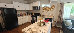 Uma cozinha moderna com armários brancos, uma geladeira preta, fogão e uma área de jantar posta com pratos e talheres.