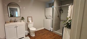 A bathroom with a toilet, sink, mirror, shower, and a small potted plant.