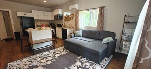 Un espacio habitable compacto con kitchenette, un sofá, una mesa de comedor y una alfombra estampada.