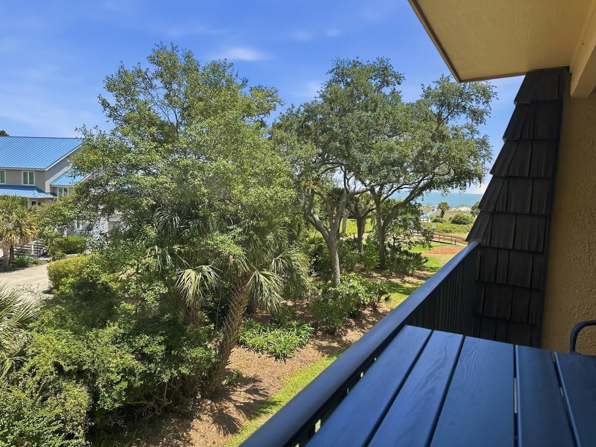 A balcony with a view of a landscaped garden and a house with a blue roof.