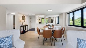 Uma sala de estar moderna com área de jantar, sofás brancos e uma grande janela com vista.
