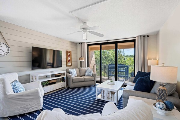 Ein Hotelzimmer mit Sofa, Sessel, Fernseher, Deckenventilator und Blick ins Freie.