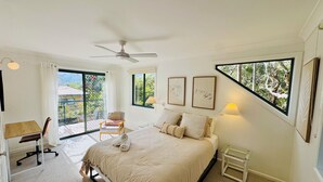 Ein Schlafzimmer mit einem Bett, einem Schreibtisch, einem Stuhl, einem Deckenventilator und großen Fenstern.