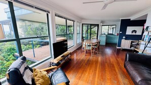Ein großzügiges Wohnzimmer mit großem Fernseher, Holzboden und einem Balkon mit Aussicht.
