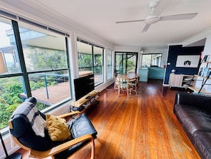 A spacious living room with a large TV, wooden flooring, and a balcony with a view.