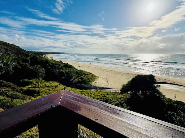A beach with a wooden walkway, ocean view, and distant hills.