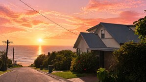 Ein Wohnhaus mit Auffahrt zur Haustür, umgeben von Grünflächen und mit Blick auf das Meer bei Sonnenuntergang.