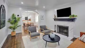 A modern living room with a fireplace, a dining area, and a kitchen in the background.