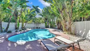 A swimming pool surrounded by lush tropical plants and a white fence.