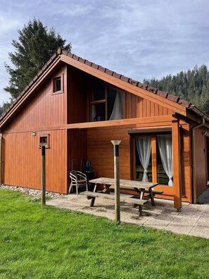 Eine Holzhütte mit einer Terrassenfläche, einem kleinen Tisch und einem Stuhl.