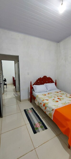 Ein Schlafzimmer mit Bett, Spiegel, Tür und einem zur angrenzenden Kammer führenden Flur.