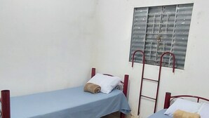 Una habitación con dos camas individuales, una ventana con rejas y suelo de baldosas.
