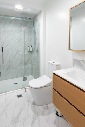 A modern bathroom with a glass-enclosed shower, a white toilet, and a wooden vanity with a mirror.