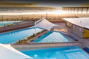 A swimming pool with a sunshade, a beach view, and a pier in the background.