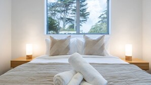 Un letto rifatto con cuscini, una finestra vista alberi e lampade da comodino.