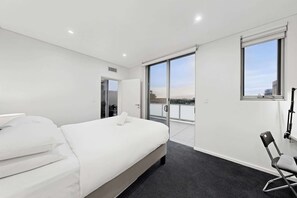 A modern hotel room with a bed, a chair, a window, and a view of the city.