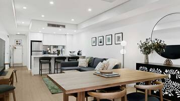 A modern kitchen with white cabinets, a dining area with a wooden table and chairs, and a living room with a sofa and a coffee table.