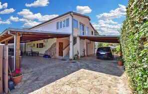 A two-story house with a covered driveway, a car parked in the driveway, and a stone patio area.