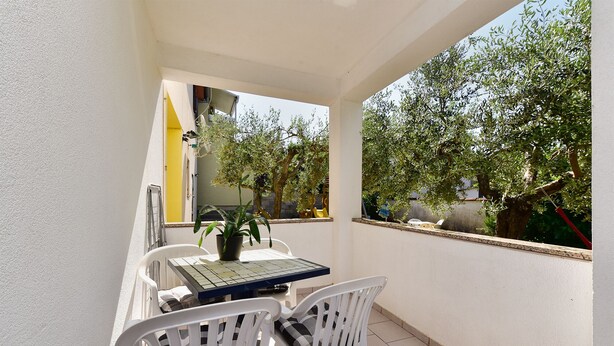 Ein Balkon mit Tisch und Stühlen, einem Blumentopf und Blick auf Bäume und ein Gebäude.