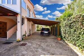 Ein Haus mit überdachter Auffahrt, einem in der Mitte geparkten Auto und einer Treppe zum Eingang.
