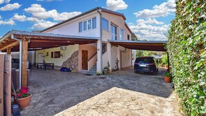 Ein zweigeschossiges Haus mit überdachter Auffahrt, einem Auto auf der Auffahrt und einer gepflasterten Terrasse.