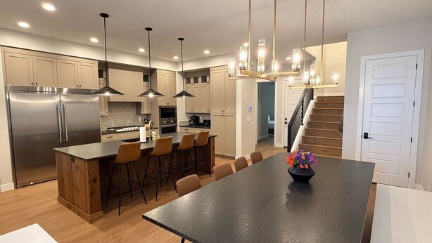 A modern kitchen with a central island, pendant lights, and a staircase leading to another level. - Elevated game-day getaway with rooftop hot tub (St. George)