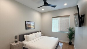 A bedroom with a bed, nightstands, a ceiling fan, a window with blinds, a potted plant, and a wall-mounted TV. - Elevated game-day getaway with rooftop hot tub (St. George)