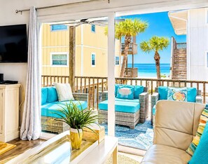 Ein Balkon mit Korbmöbeln, einem Fernseher und Blick auf Strand und Meer.