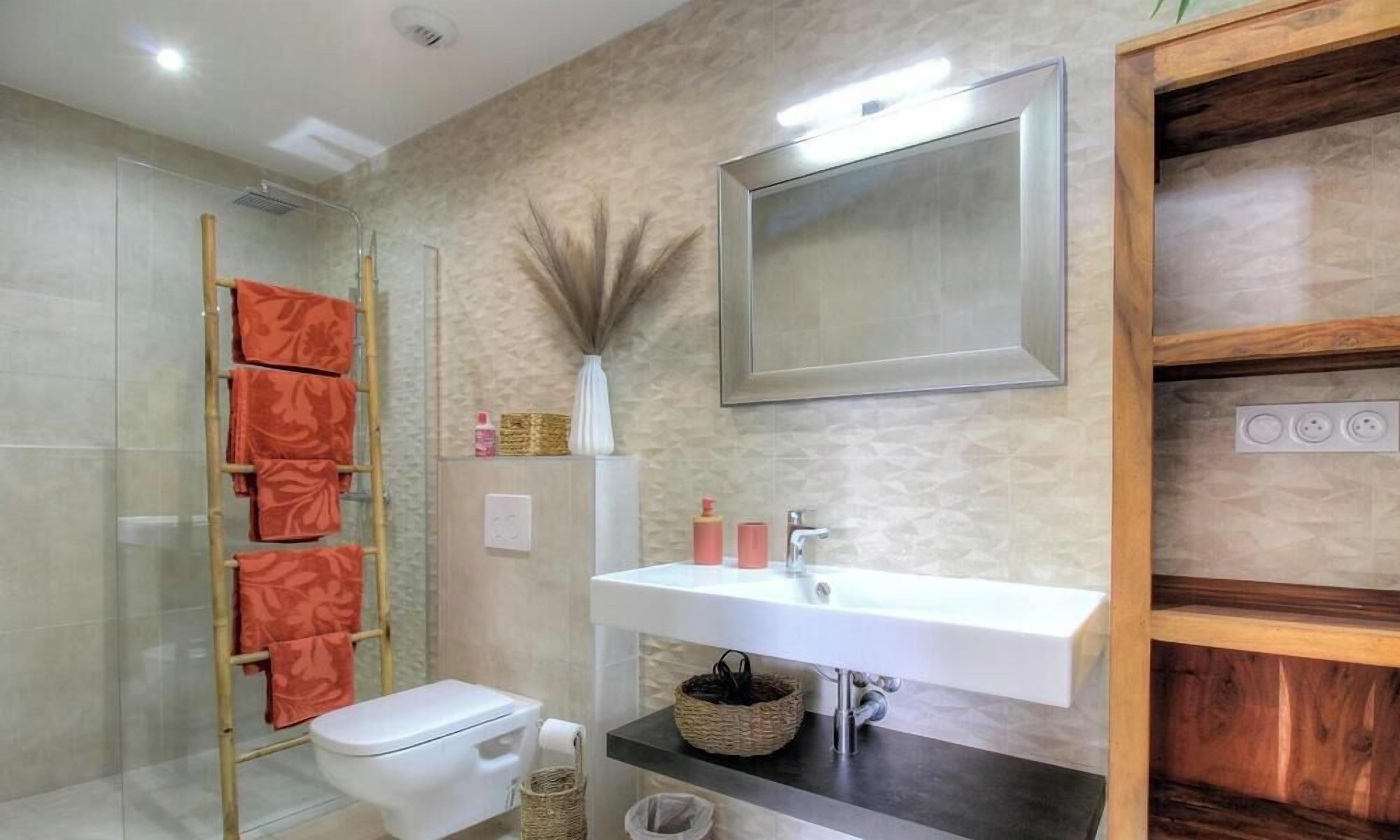A bathroom with a toilet, sink, shower, and a mirror.