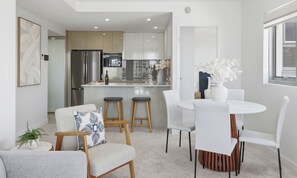 A modern kitchen with a central island, white dining chairs, and a small round table. - Verve on Sixth (Maroochydore)