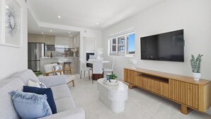 Un salon moderne comprenant un canapé, un téléviseur, une console en bois et un coin repas avec des chaises et une table.