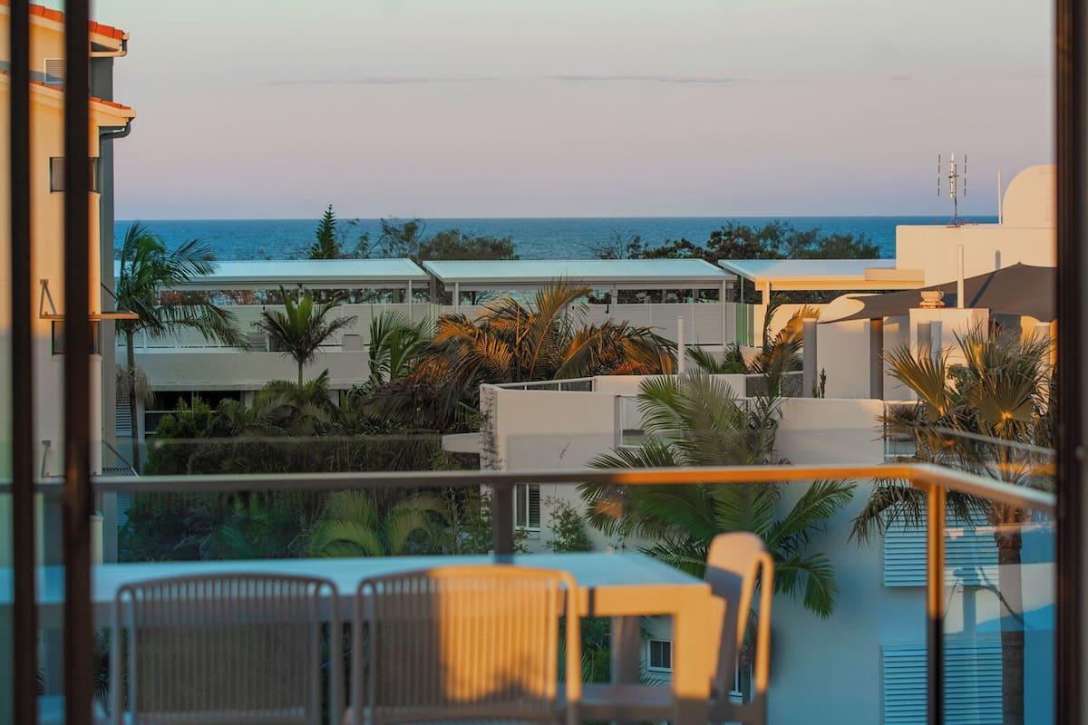 Vista a la piscina con una vista despejada del océano, una zona de estar con sillones y un edificio de techo plano.