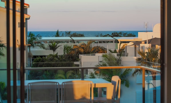 A poolside view with a clear view of the ocean, a lounge area with chairs, and a building with a flat roof.