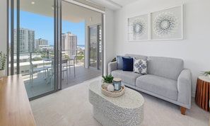 Ein modernes Wohnzimmer mit einem grauen Sofa, einem Couchtisch mit Dekoration und einem Balkon mit Blick auf Gebäude.