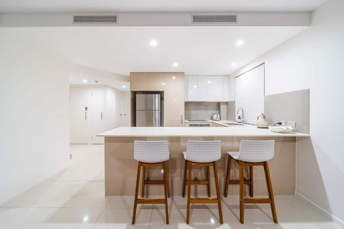 Una cocina moderna con una isla central, tres taburetes de bar y electrodomésticos de acero inoxidable.
